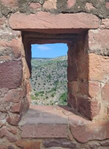 Ventana antigua en castillo, con montañas al fondo y cielo despejado.